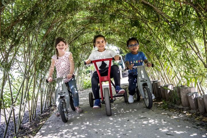 Drie kindjes op kleine fietsjes op de speelplaats van Hoedjes van Papier.